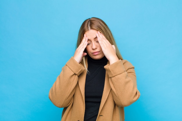 Jonge blondevrouw die beklemtoond en gefrustreerd kijken, werkend onder druk met een hoofdpijn en verontrust met problemen over muur