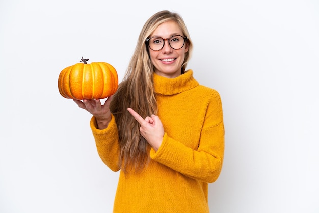 Jonge blondevrouw die een pompoen houden die op witte achtergrond wordt geïsoleerd en het richt