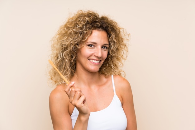 Jonge blondevrouw die met krullend haar haar tanden poetsen