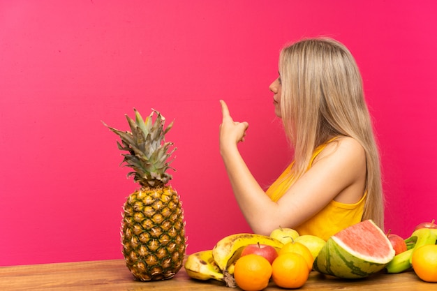 Jonge blondevrouw die met veel vruchten terug met de wijsvinger wijzen