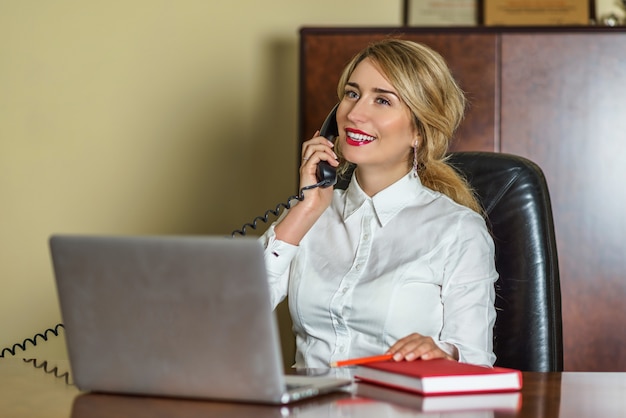 Jonge blondevrouw die op de telefoon op het kantoor spreken