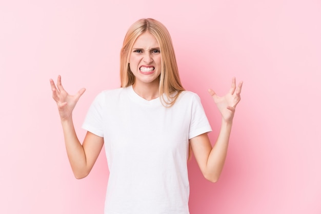 Jonge blondevrouw die op roze muur met woede gillen.