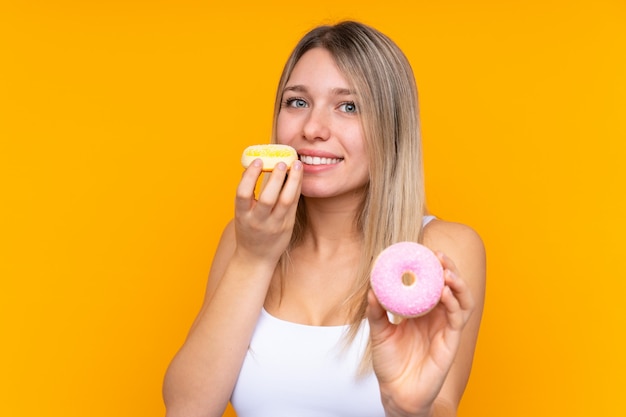 Jonge blondevrouw die over geïsoleerde blauwe muur een doughnut houden