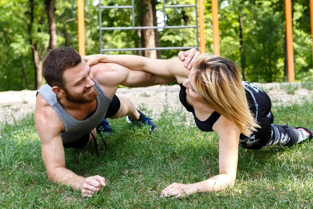 Jonge blondevrouw en gebaarde man die oefeningsplank in een park samen doen.