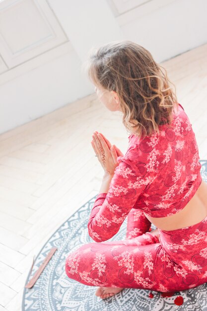 Jonge blondevrouw in rode etnische kostuum het praktizeren yogaasana namaste in lichte studio