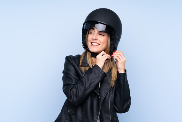 Jonge blondevrouw met een motorhelm over geïsoleerde blauwe muur