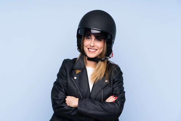 Jonge blondevrouw met een motorhelm over geïsoleerde blauwe muur