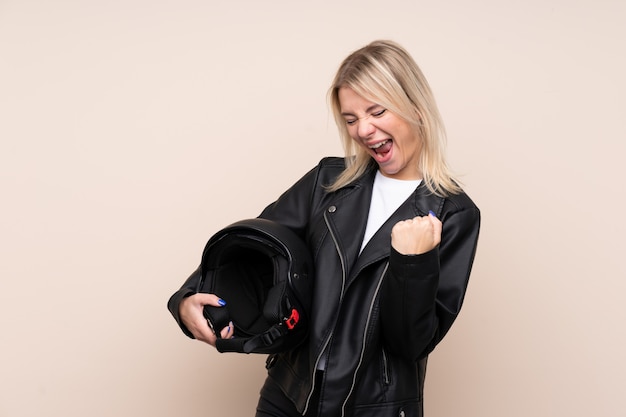 Jonge blondevrouw met een motorhelm over geïsoleerde muur die een overwinning vieren