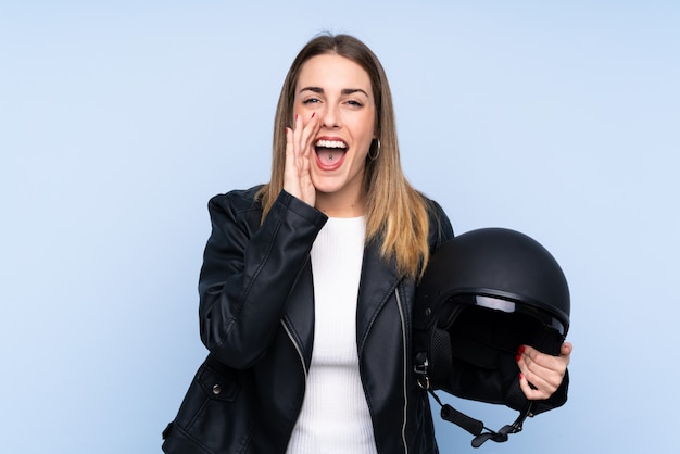 Jonge blondevrouw met een motorhelm over geïsoleerde muur die met wijd open mond schreeuwen