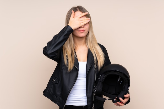 Jonge blondevrouw met een motorhelm over geïsoleerde muur die ogen behandelen door handen