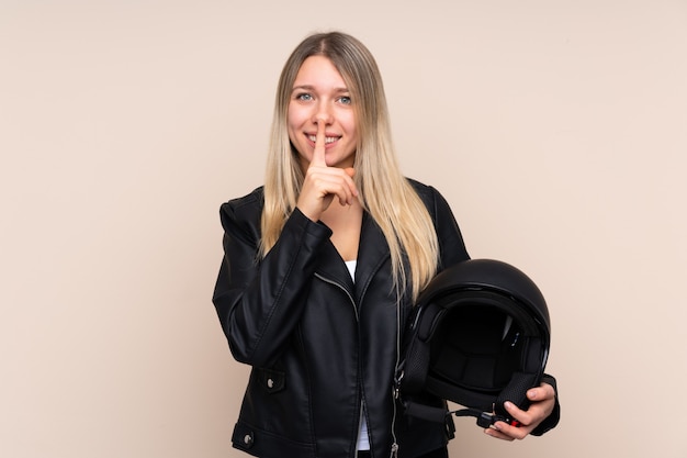 Jonge blondevrouw met een motorhelm over geïsoleerde muur die stiltegebaar doet