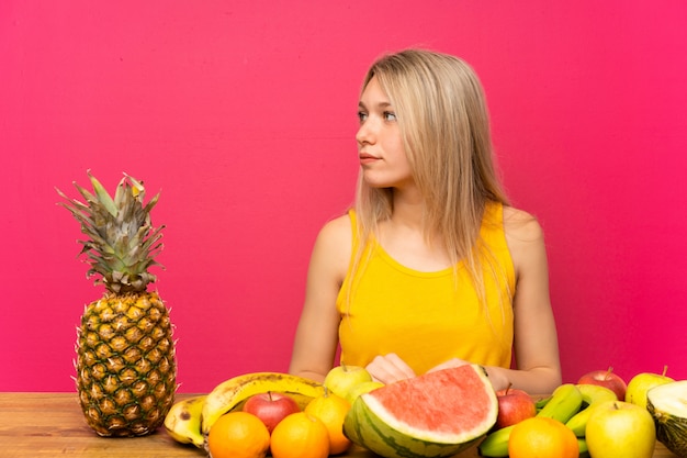 Jonge blondevrouw met veel vruchten die kant kijken