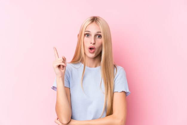 Jonge blondevrouw op roze achtergrond die één of ander groot idee, concept creativiteit hebben.