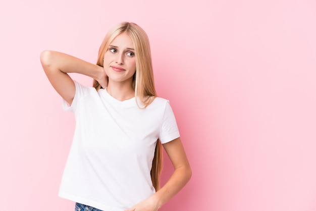 Jonge blondevrouw op roze muur wat betreft achterhoofd, denkend en makend een keuze.