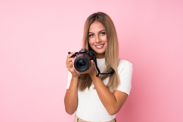 Jonge blondevrouw over geïsoleerd roze met een professionele camera