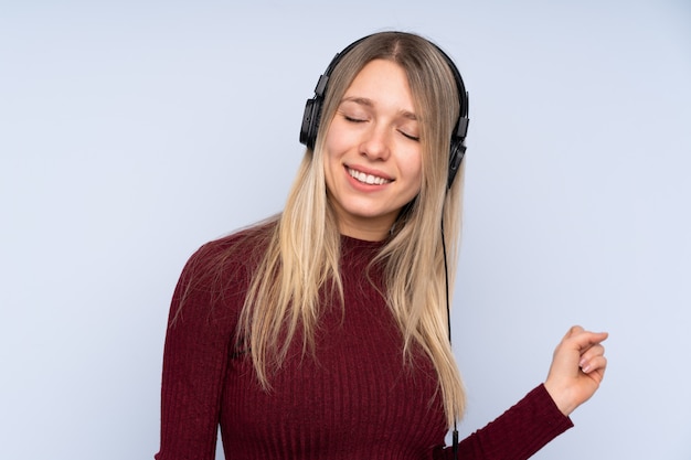 Jonge blondevrouw over geïsoleerde blauwe muur het luisteren muziek