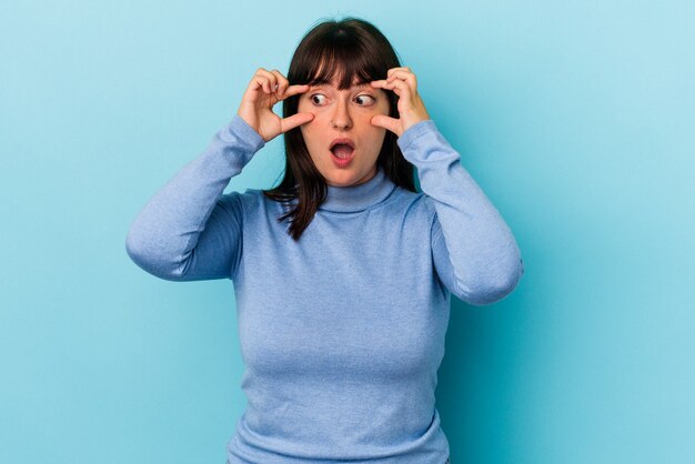 Jonge bochtige blanke vrouw geïsoleerd op blauwe achtergrond die ogen open houdt om een succeskans te vinden.