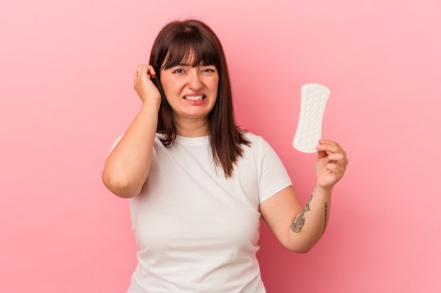 Jonge bochtige blanke vrouw met kompres geïsoleerd op roze achtergrond die oren bedekt met handen.