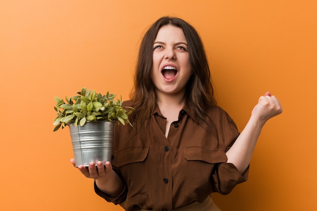 Jonge bochtige plus-maat vrouw die een plant zorgeloos en opgewonden houdt