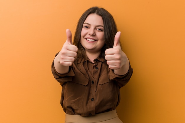 Jonge bochtige Russische vrouw met duim omhoog, proost over iets, steun en respect.