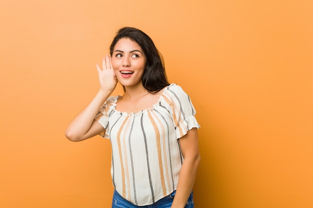 Jonge bochtige vrouw die aan een roddel probeert te luisteren.