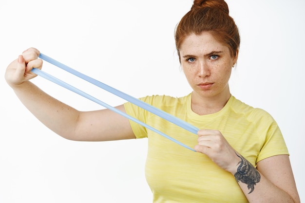 Foto jonge bochtige vrouw die de training van de weerstandsband met elastisch touw uitrekt en fitnessoefeningen doet op witte achtergrond