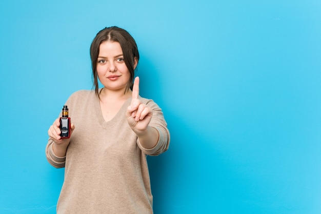 Jonge bochtige vrouw die een verdamper houdt die nummer één met vinger toont.