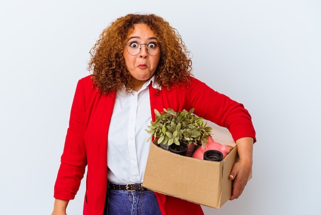 Jonge bochtige vrouw verhuizen naar een nieuw huis geïsoleerd op een witte achtergrond haalt schouders op en open ogen verward.