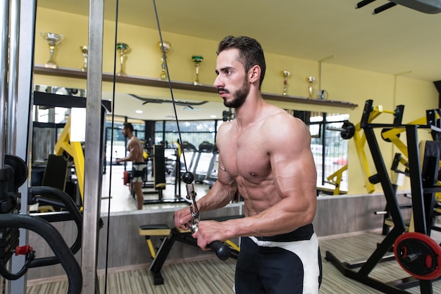 Jonge bodybuilder oefent triceps uit in de sportschool, hij voert twee armtriceps push-downs uit