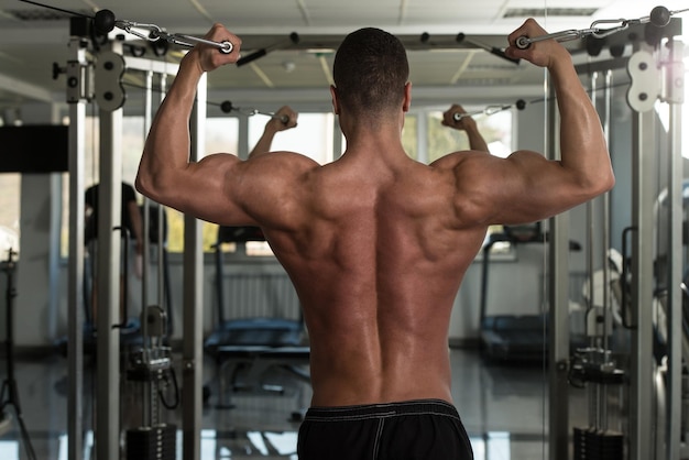 Jonge bodybuilder werkt aan zijn biceps met kabelovergang in een donkere sportschool