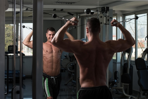 Jonge bodybuilder werkt aan zijn biceps met kabelovergang in een donkere sportschool