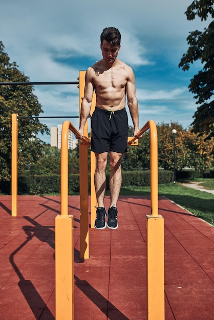 Jonge bodybuilder zonder shirt die tijdens zijn workout op parallelle balken duikt in een calisthenicspark