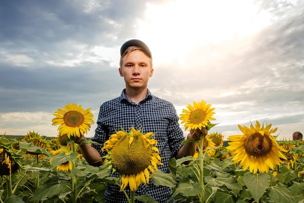 Jonge boer die in zonnebloemveld staat en gewas onderzoekt bij zonsondergang en naar de camera kijkt