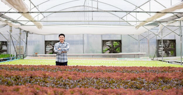 Jonge boer staat met zijn armen over elkaar op een biologische groenteboerderij met een glimlach. Moderne biologische en hydrocultuur boerderij.