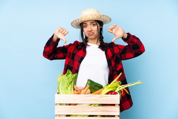 Jonge boer Vrouw met verse groenten in een houten mandje met duim omlaag
