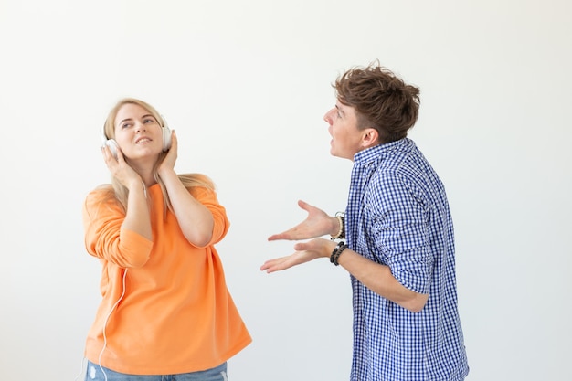 Jonge boos man smeekt zijn vrouw om naar hem te luisteren, maar ze luistert naar muziek met een koptelefoon poseren op een