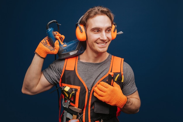 Jonge bouwer glimlacht terwijl het hebben van apparatuur in de arm