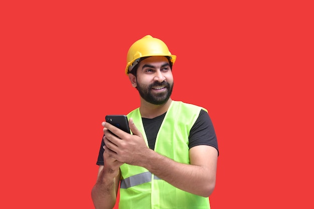 jonge bouwvakker die lacht en de telefoon vasthoudt met beide handen Indisch Pakistaans model