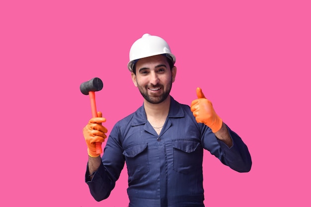 jonge bouwvakker glimlachend met duim omhoog teken en hamer Indiase Pakistaanse model te houden