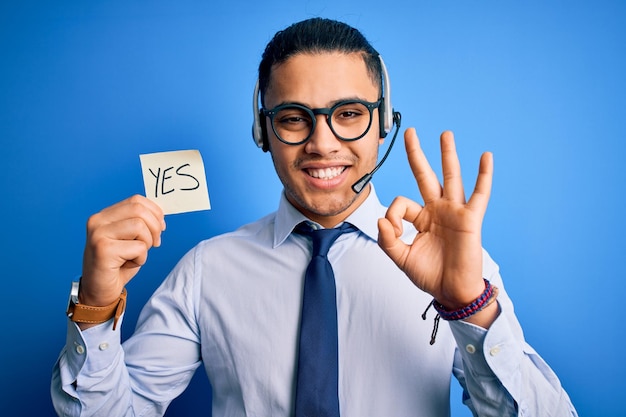 Jonge braziliaanse callcenter agent man met herinneringspapier met ja bericht ok teken doen met vingers uitstekend symbool