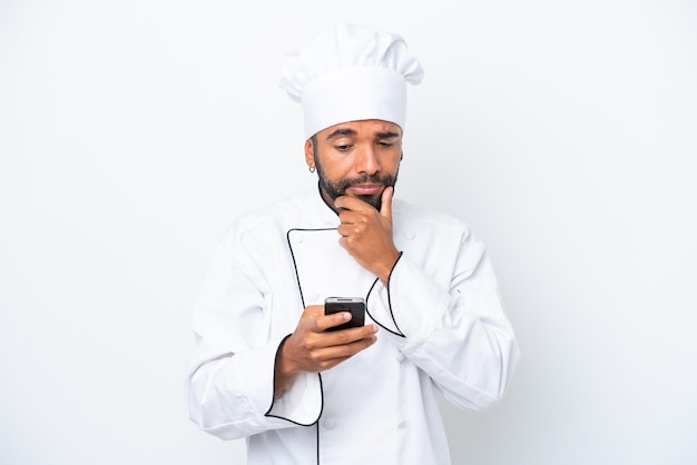 Jonge Braziliaanse chef-kok man geïsoleerd op een witte achtergrond denken en het verzenden van een bericht