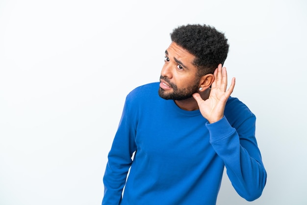 Jonge Braziliaanse man geïsoleerd op een witte achtergrond luisteren naar iets door hand op het oor te leggen