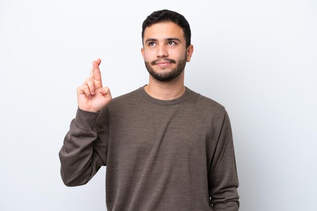 Jonge Braziliaanse man geïsoleerd op een witte achtergrond met vingers die kruisen en het beste wensen