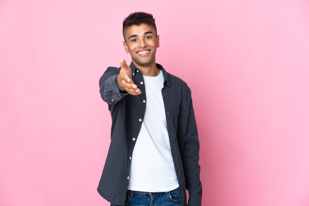 Jonge Braziliaanse man geïsoleerd op roze muur handen schudden voor het sluiten van een goede deal