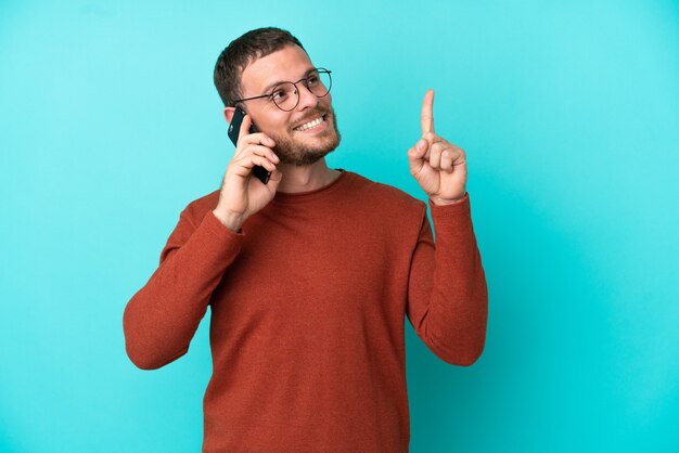 Jonge braziliaanse man met behulp van mobiele telefoon geïsoleerd op een blauwe achtergrond die een geweldig idee benadrukt