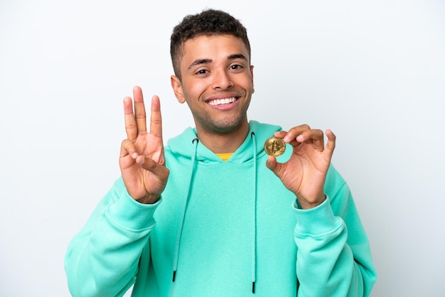 Jonge Braziliaanse man met een Bitcoin geïsoleerd op een witte achtergrond gelukkig en drie tellen met vingers