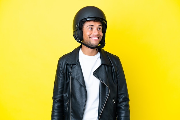 Jonge Braziliaanse man met een motorhelm geïsoleerd op een gele achtergrond die een idee denkt terwijl hij omhoog kijkt