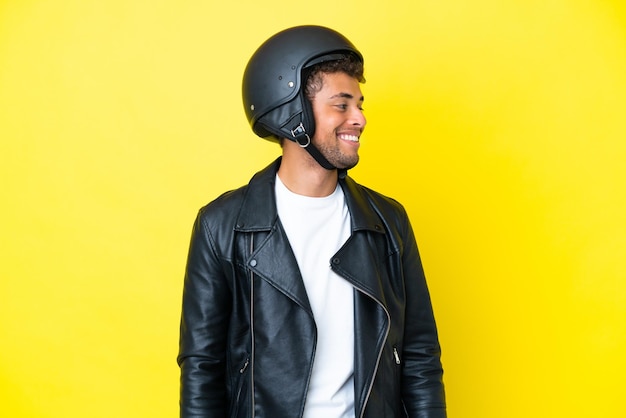 Jonge Braziliaanse man met een motorhelm geïsoleerd op een gele achtergrond op zoek naar de zijkant