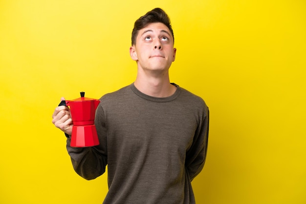 Jonge Braziliaanse man met koffiepot geïsoleerd op gele achtergrond en opzoeken