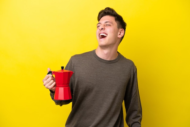 Jonge Braziliaanse man met koffiepot geïsoleerd op gele achtergrond lachen